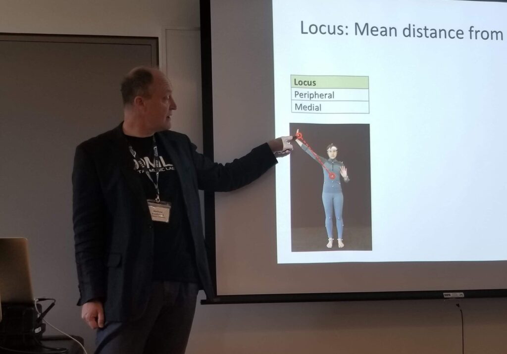 Dr. Matthew Woolhouse pointing to a picture on the slide he is presenting to a group of attendees at ICMPC 2018.